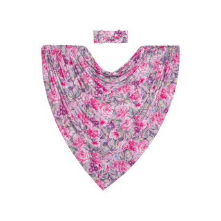 The Posh Peanut Bamboo Swaddle and Headwrap Set - Ellery (Floral) features a triangular draped floral print with pink and purple roses, green leaves on soft bamboo viscose, and a matching headwrap. The background is solid green.