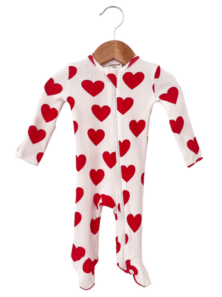 A SpearmintLOVE Organic Waffle 2-Way Zip Footie in white with red hearts, featuring long sleeves, footed bottoms, and a convenient two-way zipper, hangs on a wooden hanger against a white backdrop.